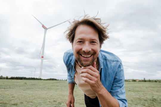Smiling man standing outdoors near wind turbine on windy day