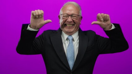 Senior man in suit smiling and pointing to himself with both thumbs against vibrant pink background, conveying confidence and pride in business setting.