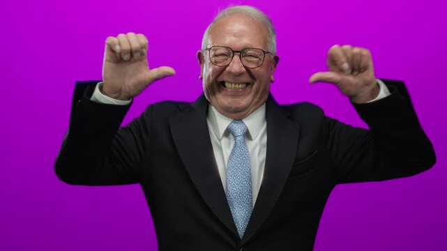 Senior man in suit smiling and pointing to himself with both thumbs against vibrant pink background, conveying confidence and pride in business setting.