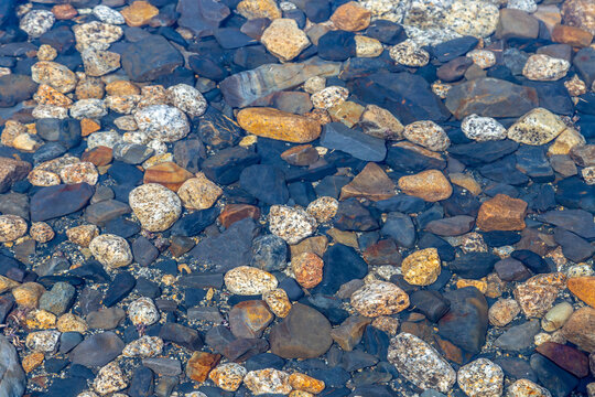 Small multi-colored stones in clear water at the bottom of a mountain lake