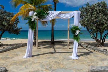 A silk-draped wedding pagoda adorned with white Phalaenopsis aphrodite orchids and lush tropical foliage stands on a Caribbean beach against the turquoise sea