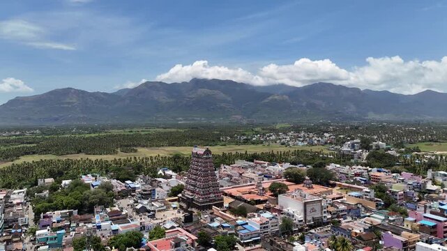 Scenic drone view of Tenkasi&rsquo;s Kasi Viswanathar Temple surrounded by vibrant town buildings, coconut fields, and the stunning Western Ghats landscape on a sunny day in Tamil Nadu.