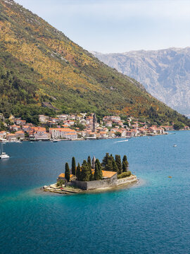 Aerial view of the serene islet of Sveti Dorde basks in the sun-drenched waters, contrasted by the rugged mountains and the quaint town nestled along the coast, Perast, Kotor Municipality, Montenegro.