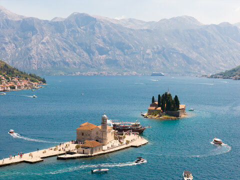 Aerial view of sun-kissed islands stand sentinel in the azure waters, framed by majestic mountains, a serene haven of history and beauty, Perast, Kotor Municipality, Montenegro.