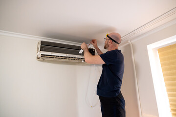 A man with a headlamp diligently repairs a wall-mounted air conditioner unit, focusing on its internal wiring and components. This image highlights home maintenance, HVAC service, or DIY repair work.