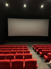Obraz premium interior of movie theater also known as a cinema. The room features large blank projection screen and rows of red upholstered seats.