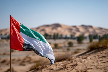 Uae flag waving in desert landscape with sand dunes and clear sky