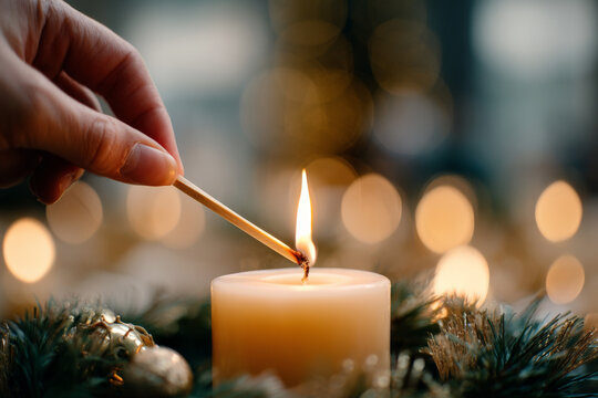 Hand lighting candle amidst holiday decorations and warm glow - Powered by Adobe