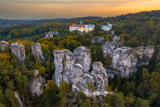 Aerial view of the majestic Hruba Skala castle perched atop sandstone formations amidst a sea of green forest under a golden sunset, Turnov, Liberec Region, Czechia.