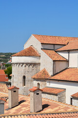 Fototapeta premium A detailed view of the terracotta tile rooftops and stone structure of the Cathedral of the Assumption of the Blessed Virgin Mary in Krk under a clear blue sky