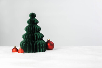 Minimal Christmas holiday background. White snow in the foreground with copy space and a minimalist Christmas tree and red ornaments.