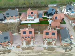 Drone inspection view of near completed first time and affordable buyer homes on a rural British housing development project. Larger, detached homes ate in the background.