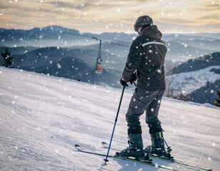 A skier stands on a snowy slope, looking out at the mountain range and ski lift on a winter day with falling snow.