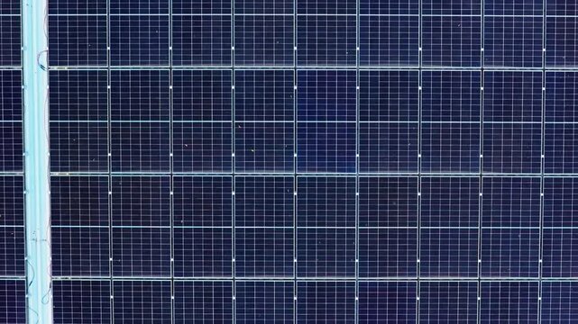 Drone moving left above solar power field on industrial building, showing geometric pattern of blue photovoltaic panels
