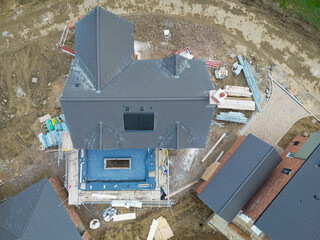 Drone inspection view of a near completed large family home showing a soon to be fitted lantern on the blue covered conservatory roof. Located on a British housing site.