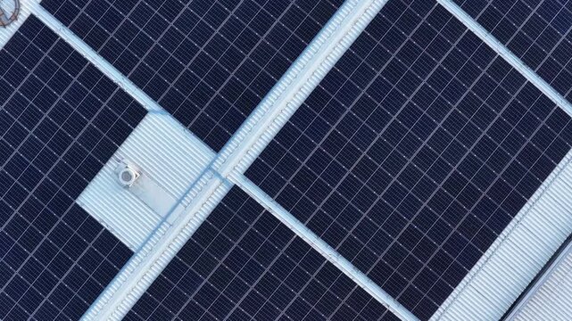 Drone ascending and rotating over solar panel array on large industrial building, modern renewable energy concept