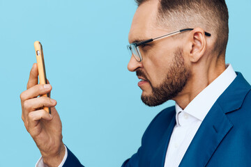 Professional businessman studies a phone with a focused expression against a solid blue background, portraying ambition, concentration, and decisive mood, his posture reflecting leadership and clear