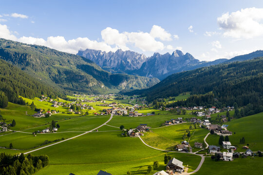Aerial view of emerald meadows meet the rugged, jagged peaks of the Dachstein Mountains, nestled within a verdant valley under a serene sky, Gosau, Upper Austria, Austria.