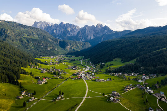 Aerial view of a verdant valley nestled between towering, jagged peaks, where sunlight kisses the emerald meadows and rustic villages dot the landscape, Gosau, Upper Austria, Austria.