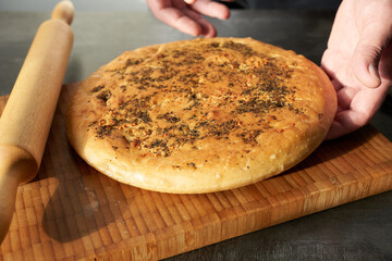 A chef prepares focaccia on a wooden board, close-up. Food preparation.