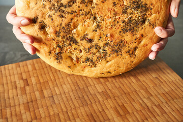 Woman holding tasty bread on wooden board, closeup. Baking concept