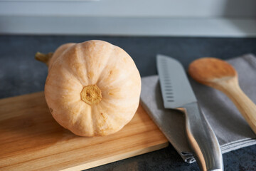 Pumpkin on a cutting board with a knife and spoon on a kitchen countertop.
