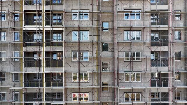 Drone panning right along residential building facade under renovation, construction scaffolding and exterior details visible