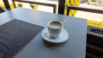 Cup of cappuccino on table near window in sunny cafe, simple lifestyle and morning relaxation concept