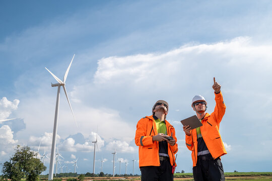 Engineers using drone and tablet for wind turbine inspection at wind farm. Two engineers (two men) operating a drone for inspecting wind turbines, concept of technology and sustainability. - Powered by Adobe
