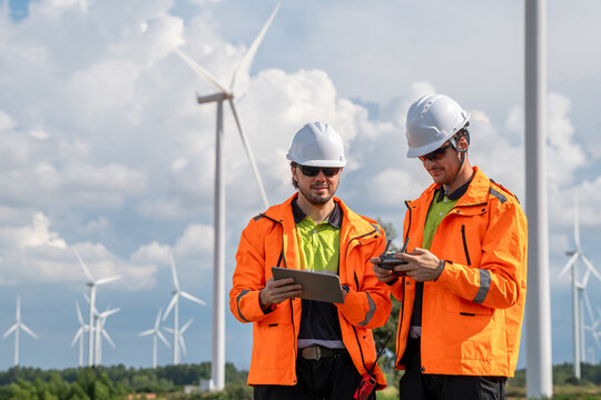Engineers using drone and tablet for wind turbine inspection at wind farm. Two engineers (two men) operating a drone for inspecting wind turbines, concept of technology and sustainability.