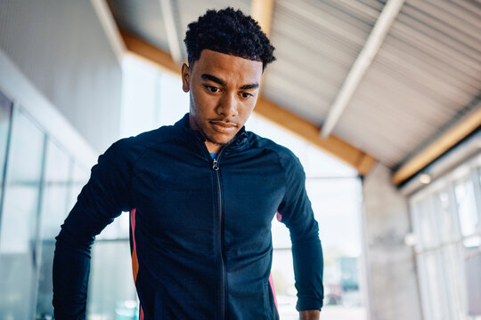 Fit young man in sports clothing looking exhausted while standing alone in a gym during a break from a workout session