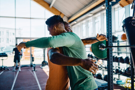 Two diverse young men in sportswear ecstatically embracing each other after a workout session together in a gym