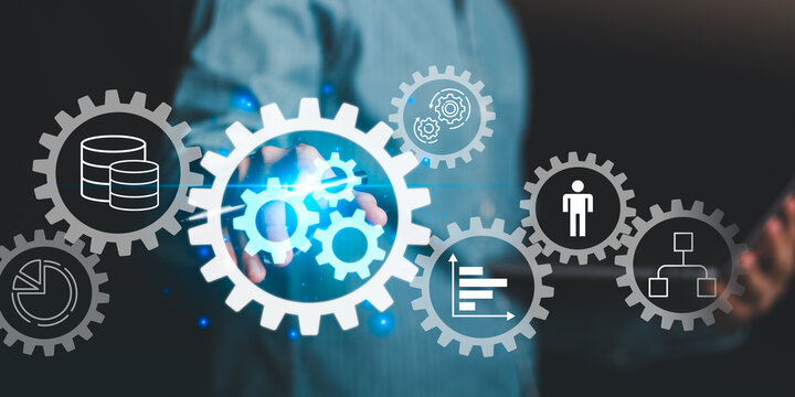 A businessman interacting with virtual gear icons representing automation, workflow, data management, and corporate efficiency in digital business technology and process improvement systems.