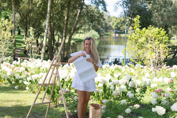 woman artist paints a picture on an easel in a garden with white blooming hydrangeas