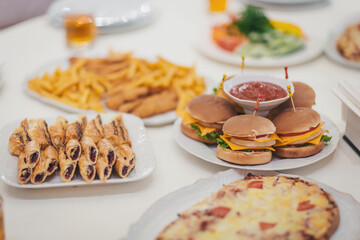 Delicious spread of various snacks including sandwiches, pastries, fries, and salads at a celebration party during the daytime