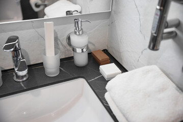 Fototapeta premium Modern hotel bathroom interior with stylish sink, marble countertop, towels, and disposable amenities. Clean and minimalistic design concept for hospitality, travel, and hygiene themes.