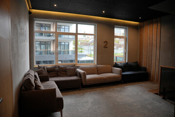A cozy, modern lobby or common area with soft lighting and comfortable sofas, featuring an industrial-chic design with wooden accents and large windows overlooking a contemporary resort complex.