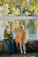 Fototapeta premium Two senior women talking by the lake in autumn