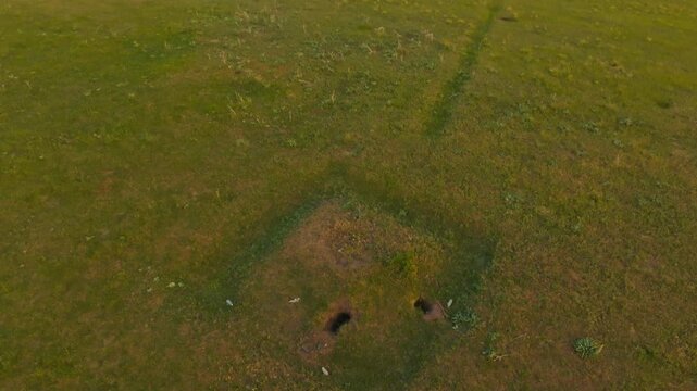 Aerial drone view of ancient kurgan mound in Chuy Valley, Kyrgyzstan. Square site with ditch, trench to mountains, fresh holes, debris.