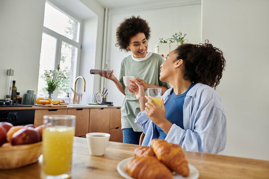 Two joyful African American women share drinks and laughter in their stylish home - Powered by Adobe