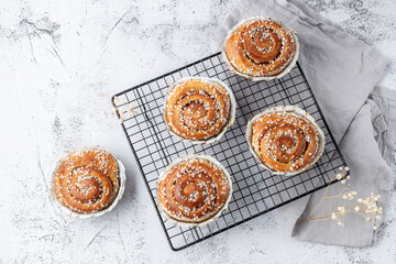 Freshly baked cinnamon buns rolls on retro metal baking rack with grey linen napkin on grunge stone table background. Traditional swedish sweet  kanelbulle.