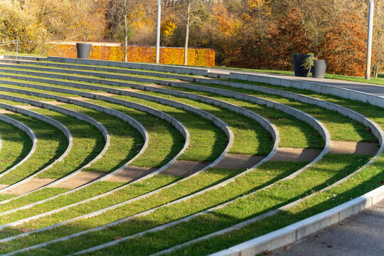 Curved amphitheater steps sweep in repeating lines of concrete and grass. Long shadows add rhythm to the minimalist scene.