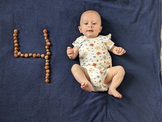 Adorable four-month-old baby celebrating a milestone, lying next to the number four made of walnuts.

