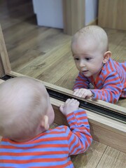 A curious baby lying on his tummy, fascinated by his own reflection in a mirror.

