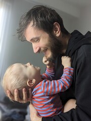 Father gently cradling his one-year-old baby's head, sharing a tender eye contact moment.

