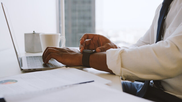 Close Up Of Businessman Working At Desk On Laptop In Modern Office Checking Data On Smart Watch