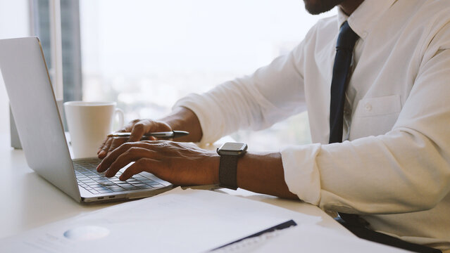 Close Up Of Businessman Wearing Smart Watch Working At Desk On Laptop In Modern Office