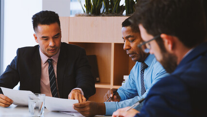 Three Businessmen Sitting Around Table Meeting In Modern Open Plan Office