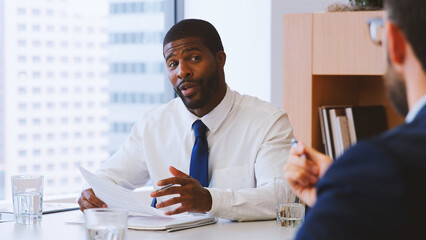 Two Businessmen Sitting Around Table Meeting In Modern Open Plan Office