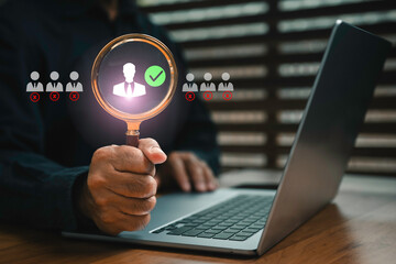 Businessman using magnifying glass to choose the right candidate on laptop, symbolizing recruitment, human resources management, employee selection, and hiring process in modern business.